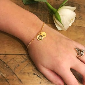 May include: A gold chain bracelet with two charms. One charm has a paw print and the other charm has the letter "R" engraved on it.