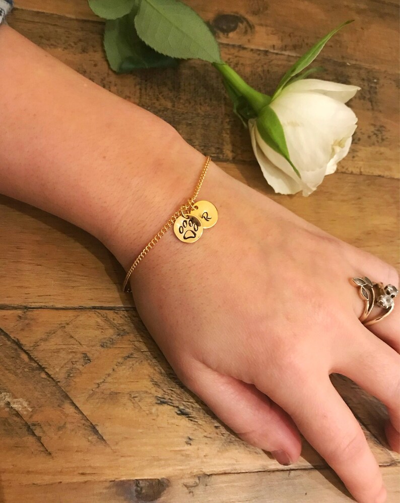 May include: A gold chain bracelet with two charms. One charm has a paw print and the other charm has the letter "R" engraved on it.