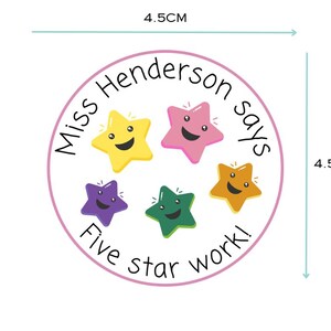 K&ouml;nnte beinhalten: Ein runder Aufkleber mit einem Durchmesser von 4,5 cm, mit einem rosa Rand und dem Text "Miss Henderson says Five star work!". Er zeigt f&uuml;nf l&auml;chelnde Sterne in Gelb, Rosa, Orange, Gr&uuml;n und Lila.