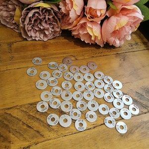 May include: A collection of silver metal discs with numbers and letters engraved on them. The discs are arranged in a random pattern on a wooden surface.