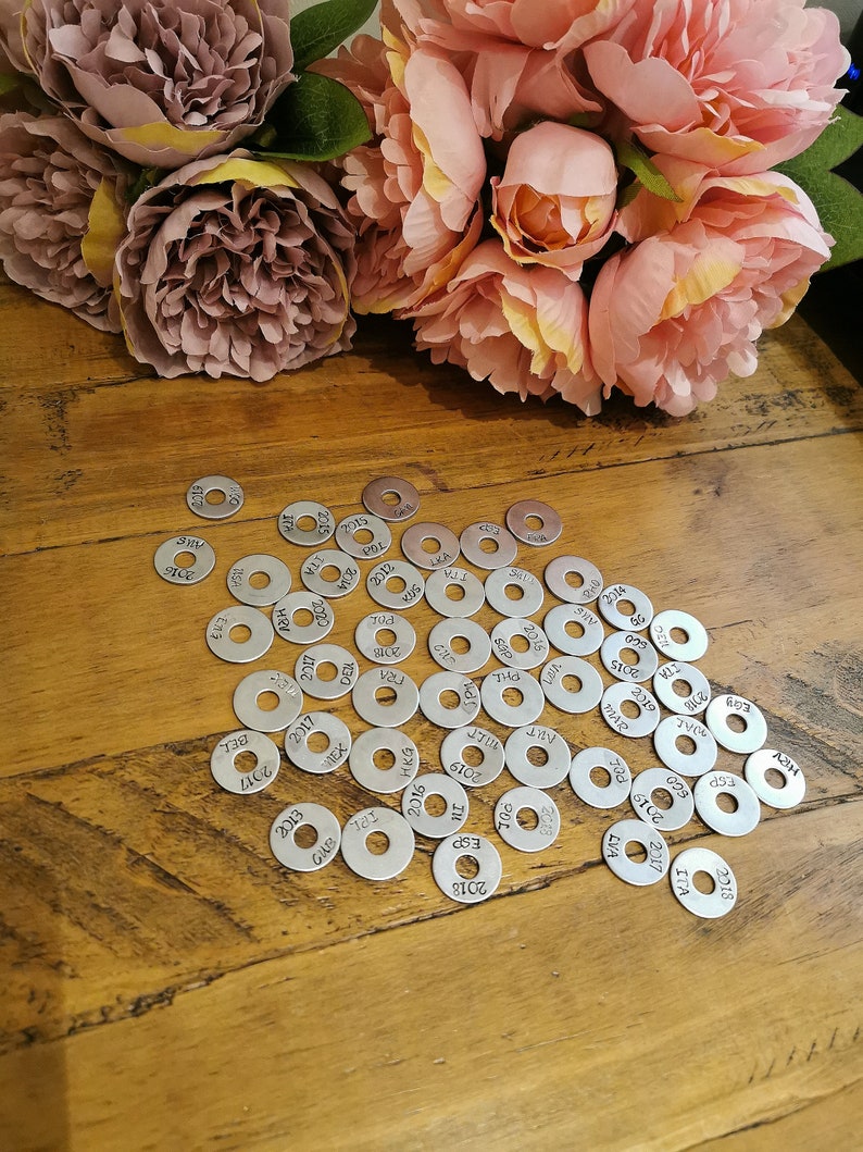 May include: A collection of silver metal discs with numbers and letters engraved on them. The discs are arranged in a random pattern on a wooden surface.