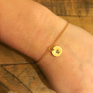 May include: A gold chain bracelet with a round charm that has the letter "R" engraved on it.