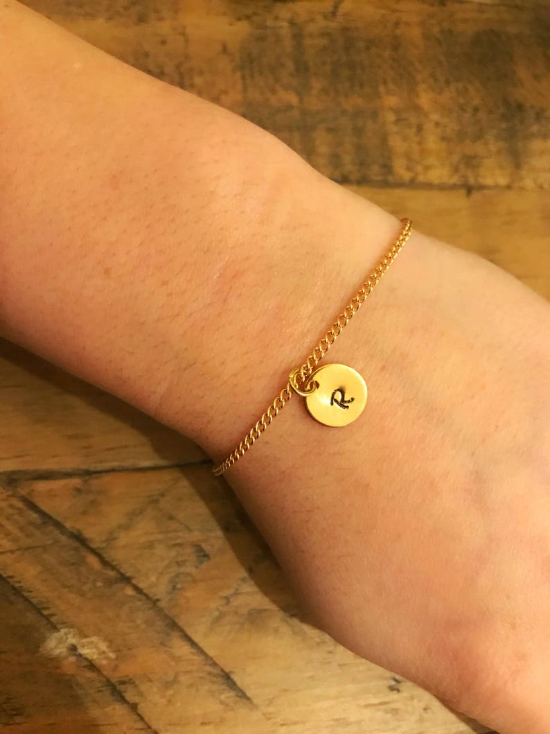 May include: A gold chain bracelet with a round charm that has the letter "R" engraved on it.