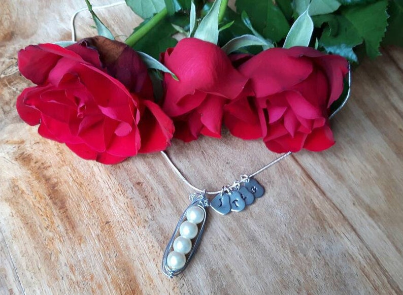 May include: A silver necklace with a pea pod charm containing four white pearls. The necklace also has five silver heart charms with the letters J, C, L, I, and E.