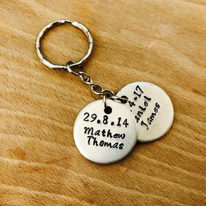 Peut inclure: Porte-cl&eacute;s en argent avec deux &eacute;tiquettes rondes en m&eacute;tal. La premi&egrave;re &eacute;tiquette dit "29.8.14 Matthew Thomas" et la deuxi&egrave;me &eacute;tiquette dit "4.4.17 Daniel James".