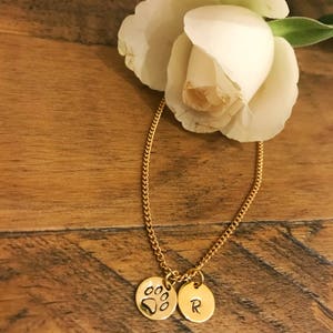 May include: A gold chain necklace with two charms. One charm is a paw print and the other charm is a letter R.