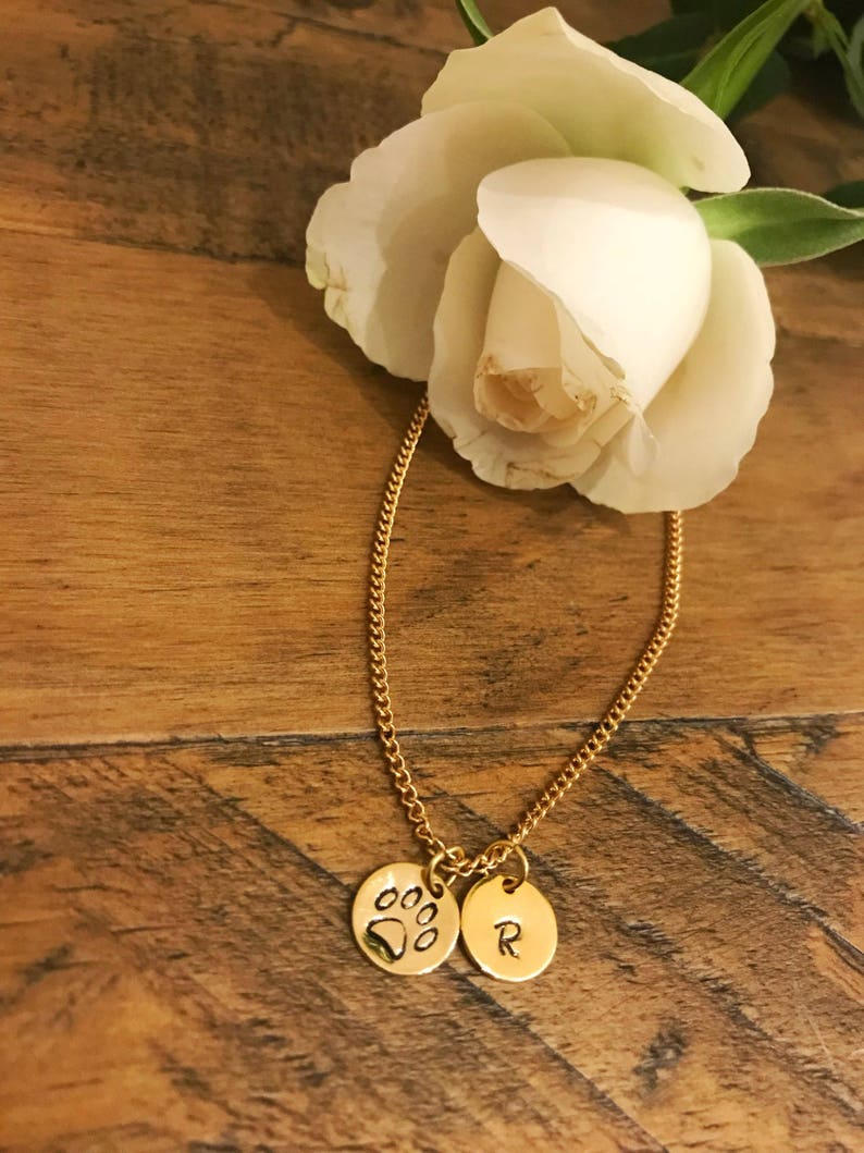 May include: A gold chain necklace with two charms. One charm is a paw print and the other charm is a letter R.