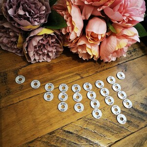 May include: A collection of silver metal discs with years and abbreviations printed on them. The discs are arranged in a semi-circle pattern on a wooden surface.