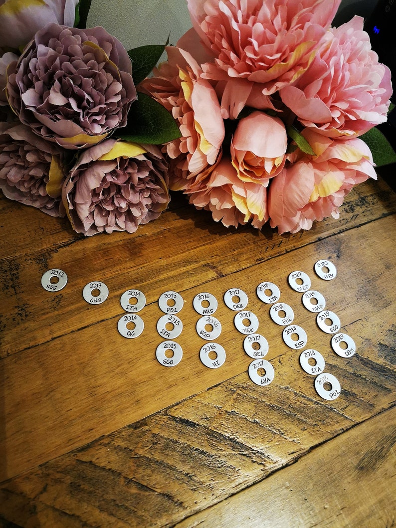 May include: A collection of silver metal discs with years and abbreviations printed on them. The discs are arranged in a semi-circle pattern on a wooden surface.