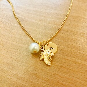May include: A gold chain bracelet with a pearl charm, a gold leaf charm, and a gold disc charm with the letter "A" engraved on it.