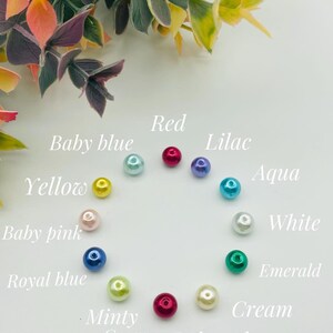 Puede incluir: Un c&iacute;rculo de 12 cuentas de perla en varios colores, incluyendo rojo, amarillo, azul, verde, blanco y crema. Las cuentas est&aacute;n etiquetadas con sus colores correspondientes.