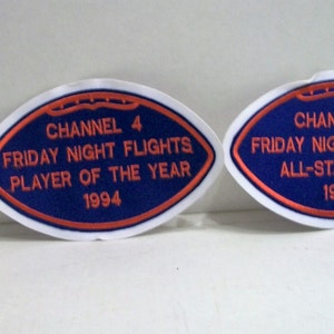 May include: Two blue and white football-shaped patches with red embroidered text. The text on the left patch reads "Channel 4 Friday Night Flights Player of the Year 1994". The text on the right patch reads "Channel 4 Friday Night Flights All-Star Team 1994".