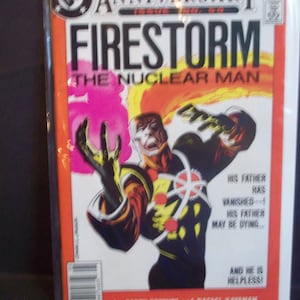 May include: A comic book cover featuring a superhero called Firestorm, the Nuclear Man. The cover is red, yellow, and black with a bright orange and yellow background. The text on the cover reads "DC Anniversary, Firestorm, The Nuclear Man, His father has vanished - His father may be dying... And he is helpless!" The cover also includes the text "by Gerry Conway and Rafael Kayanan".