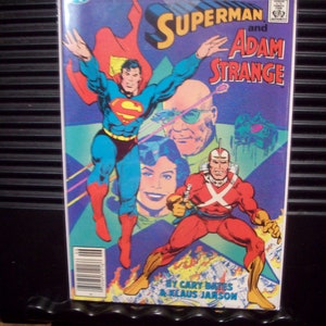 May include: A comic book cover featuring Superman and Adam Strange. Superman is in a blue suit with a red cape, and Adam Strange is in a red and yellow suit. The cover has the text "DC Comics Presents" and "Superman and Adam Strange".