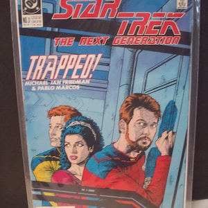 May include: A Star Trek: The Next Generation comic book cover featuring a red, blue, and yellow illustration of three characters trapped in a room. The title of the comic is "Trapped!" and the issue number is 3.