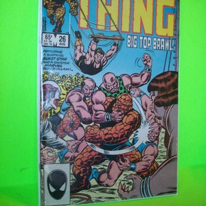 Könnte beinhalten: Ein Comic-Cover mit The Thing von den Fantastic Four. Das Cover ist blau und gelb mit dem Titel "The Thing" in großen gelben Buchstaben. The Thing ist in einem Wrestling-Match mit einem großen, muskulösen Mann dargestellt. Der Covertext lautet "Big Top Brawl!" und "Featuring a surprise guest star and a sinister Marvel super-villain!"