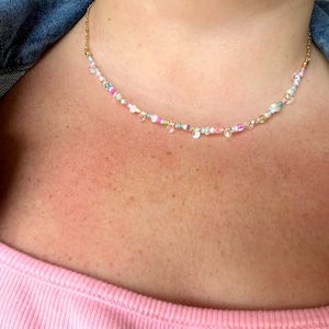 May include: A delicate necklace featuring a thin gold-toned chain interspersed with small, multicolored beads in shades of pink, blue, white, and green, accented by tiny, clear, teardrop-shaped charms hanging at intervals along the length.