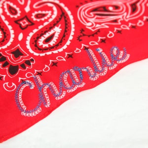 May include: Red bandana with a paisley pattern and the name "Charlie" embroidered in white and blue thread.