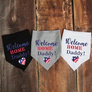 May include: Three fabric bandanas with the text "Welcome Home Daddy!" in blue and red lettering. Each bandana features a red, white, and blue heart with a star pattern. The bandanas are black, gray, and white.