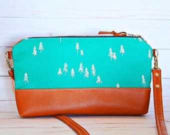 May include: A turquoise zippered pouch with a brown leather bottom and a white tree pattern. The pouch has a brown leather strap with gold-colored hardware.