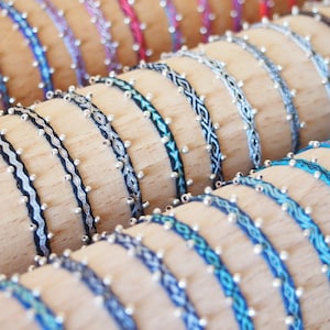 Peut inclure: Gros plan sur plusieurs bracelets colorés avec des perles argentées. Les bracelets sont tissés avec des fils de différentes couleurs et sont présentés sur des bobines en bois.