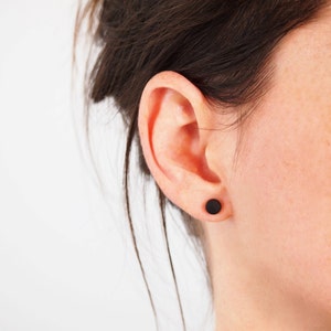 Könnte beinhalten: Nahaufnahme eines Ohrs mit einem kleinen schwarzen Ohrstecker.
