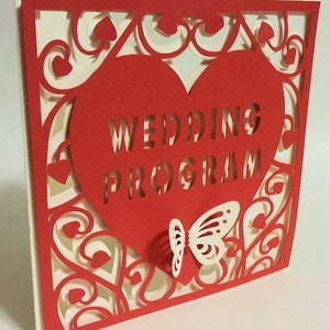 May include: Red cardstock wedding program with a white butterfly and a heart-shaped cutout that says "Wedding Program".