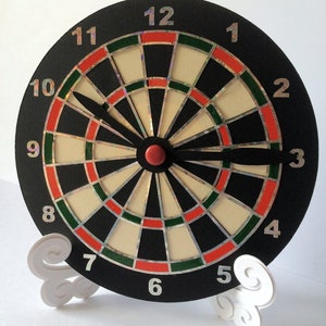 May include: A black and white dartboard with red and green accents. The numbers 1 through 12 are printed around the board. The board is on a white stand with a cloud-like design.