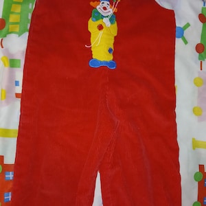 May include: Red corduroy overalls with a clown applique and the name "Kevin" embroidered on the front.