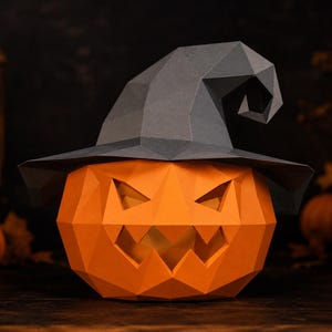 Könnte beinhalten: Ein Low-Poly-Papierkürbis mit einer geometrischen orangefarbenen Oberfläche und einem gezackten, ausgeschnittenen Gesicht. Der Kürbis trägt einen dunkelgrauen, spitzen Hexenhut mit einer gefalteten, kantigen Krempe aus Papierpaneelen.