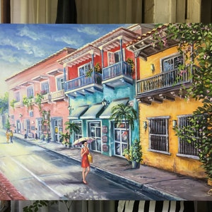 May include: A colorful painting of a street scene in a tropical city. The buildings are painted in bright colors, including yellow, pink, blue, and green. There are balconies with plants and flowers. A woman in a red dress walks down the street with a yellow umbrella. The sky is blue with white clouds.