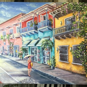 May include: A colorful painting of a street scene in a tropical city. The buildings are painted in bright colors, including pink, yellow, blue, and green. There are balconies with railings and potted plants. A woman in a red dress walks down the street with an umbrella. The street is paved with cobblestones and there is a white line down the center.