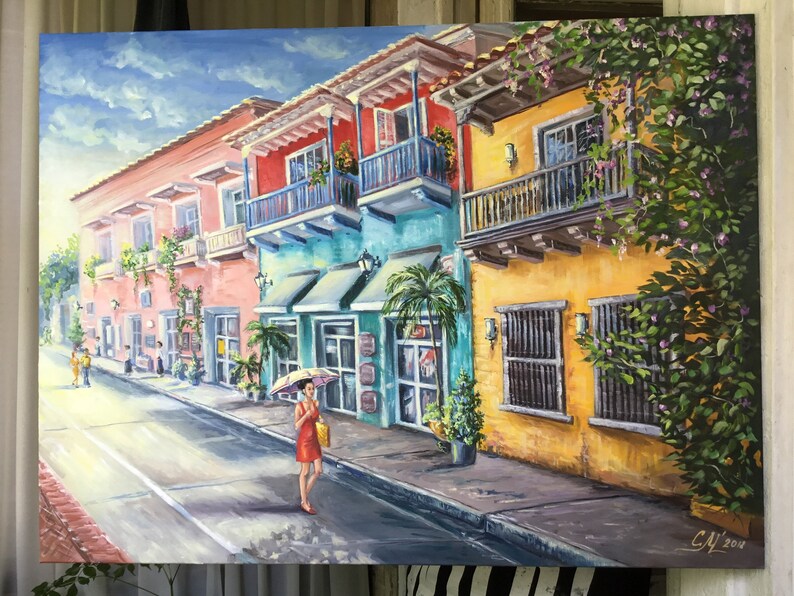 May include: A painting of a colorful street scene in a tropical city. The buildings are painted in shades of pink, yellow, blue, and green. There are balconies with plants and flowers. A woman in a red dress walks down the street with an umbrella. The painting is signed "C.M. 2014".