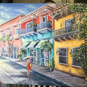 May include: A painting of a colorful street scene in a tropical city. The buildings are painted in shades of yellow, pink, blue, and green. There are balconies with railings and lush green plants growing on the walls. A woman in a red dress walks down the street with an umbrella.