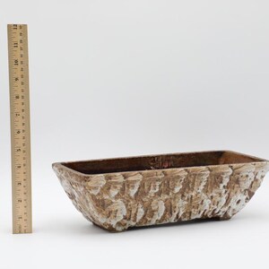 May include: A rectangular planter with a textured, bark-like appearance. The planter is brown with white accents and measures approximately 12 inches in length. A wooden ruler is positioned next to the planter.
