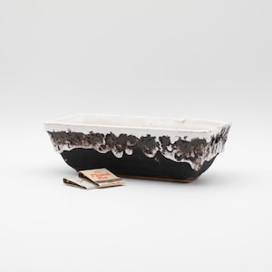 May include: Rectangular ceramic planter with a black base and white rim. The rim has a textured, dripped brown design. Two small matchbooks are in front of the planter. The planter is suitable for succulents or small plants.
