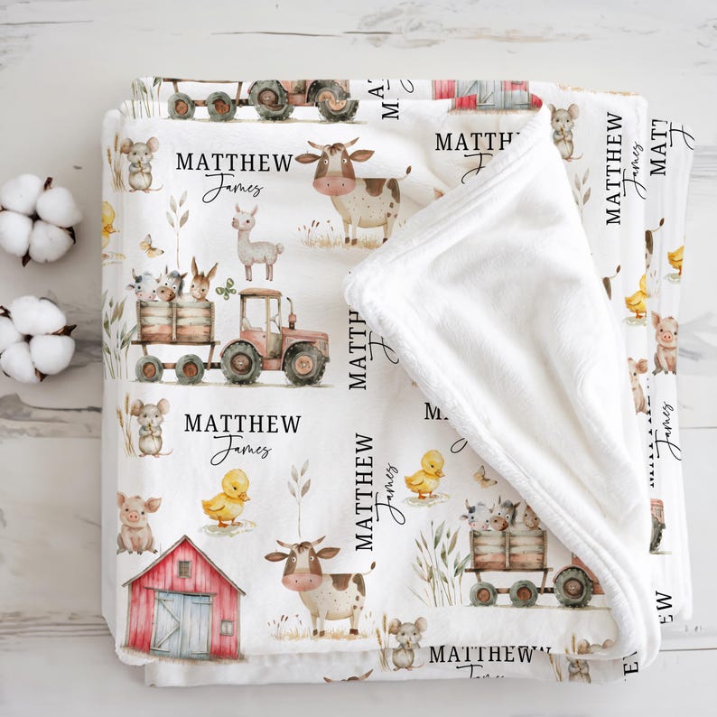 May include: A white baby blanket with a farm animal theme. The blanket features illustrations of a tractor, cows, pigs, ducks, and other farm animals. The name "MATTHEW James" is printed on the blanket in a script font.