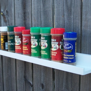 May include: A white shelf with eight spice jars. The jars are labeled with different spices, including "Spice Supreme", "5th Season", "Ground Cinnamon", "Whole Oregano", "Cayenne Pepper", "Crushed Pepper", "Medal Oregano", and "Sierra".
