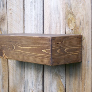 May include: A dark brown wooden shelf with a rustic finish. The shelf is mounted on a wood wall.