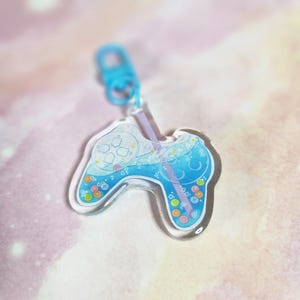 May include: A blue and white clear acrylic keychain shaped like a video game controller with a straw and colorful bubbles inside.
