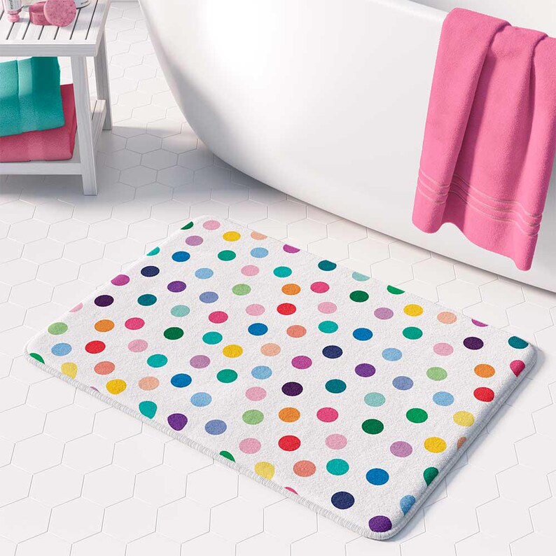 A bathroom with a white bathtub, a colorful polka dot bath mat, and a pink towel hanging on a rack.