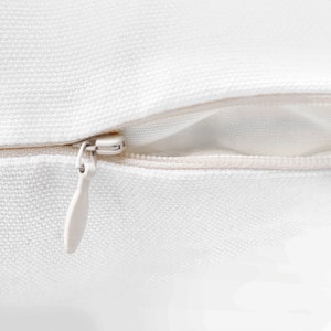 May include: Close-up of a white zipper on a pillow cover. The zipper is open and the fabric is smooth.