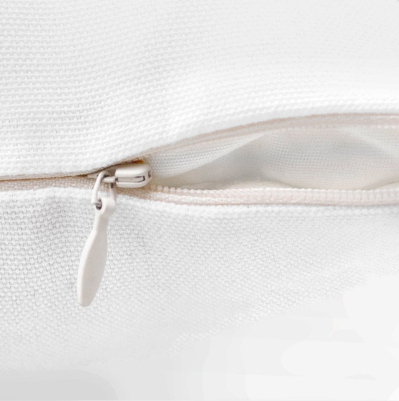 May include: Close-up of a white zipper on a pillow cover. The zipper is open and the fabric is smooth.