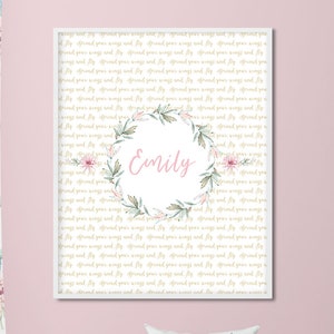 May include: A framed print with a light pink background and gold text repeating the phrase "spread your wings and fly." The center features a floral wreath with the name "Emily" in pink script.