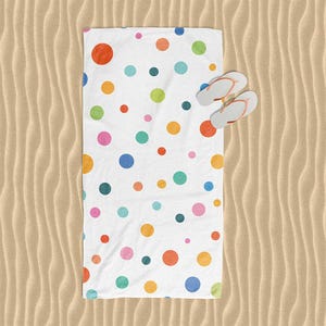 A colorful polka dot towel is spread out on a sandy beach, with a pair of flip-flops placed on top of it.
