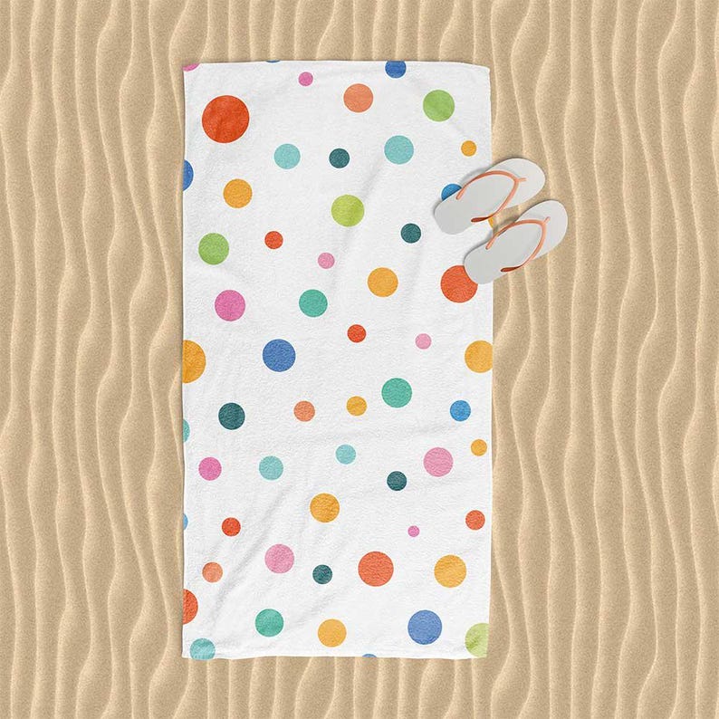 A colorful polka dot towel is spread out on a sandy beach, with a pair of flip-flops placed on top of it.