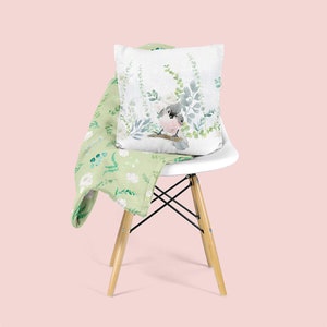 May include: A white chair with a green floral patterned throw blanket and a white pillow with a watercolor illustration of a bird on a branch with green leaves.