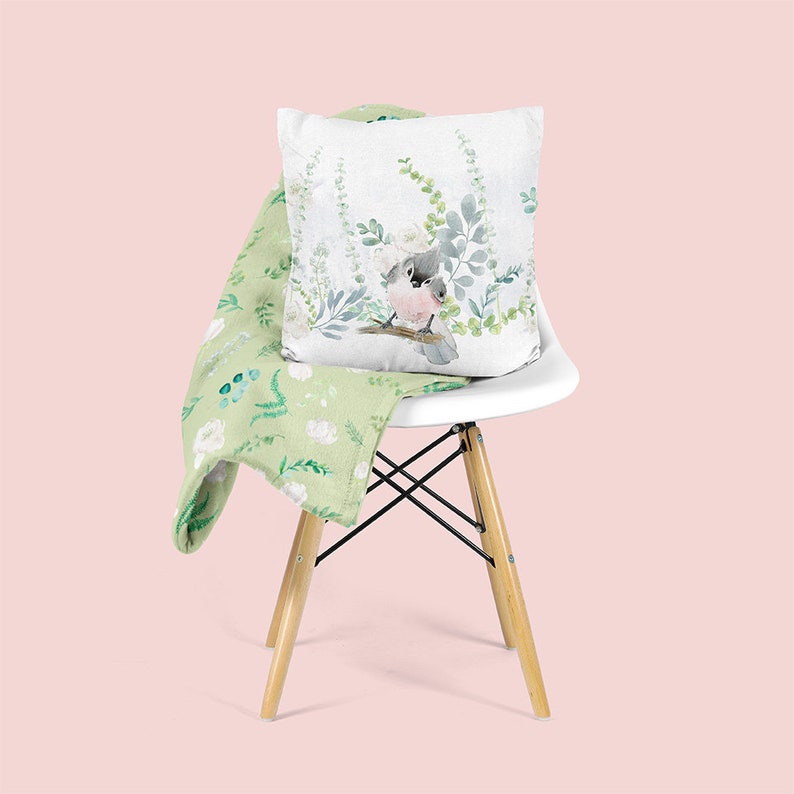 May include: A white chair with a green floral patterned throw blanket and a white pillow with a watercolor illustration of a bird on a branch with green leaves.