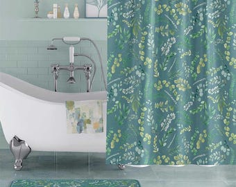 May include: A shower curtain and matching bath mat featuring a repeating watercolor pattern of green and teal eucalyptus leaves, ferns, and small white flowers on a muted teal background, displayed in a bathroom setting with a white clawfoot tub.