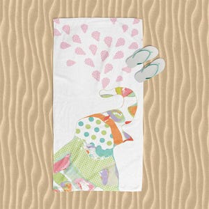 A colorful beach towel with a pattern of polka dots and a playful elephant design, along with a pair of flip-flops, is placed on a sandy beach.